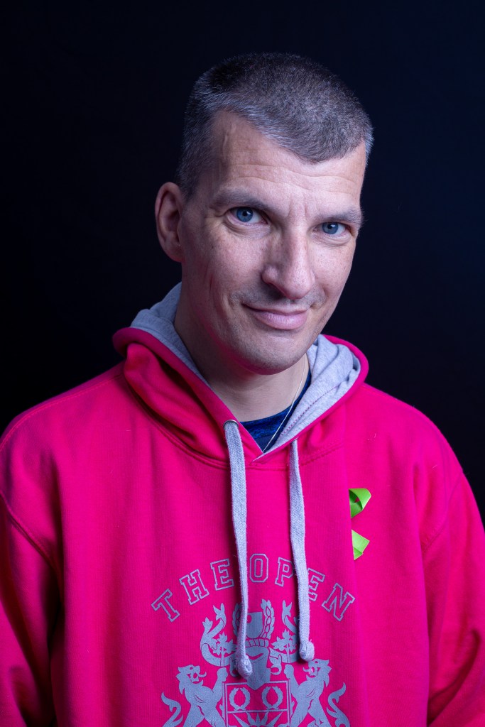 Photo of HIVBlogger with a pink Open University hoodie on with a green mental health ribbon on. 